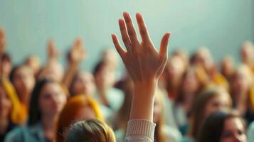 A hand raised high above a blurred audience, showing engagement in a learning environment. photo