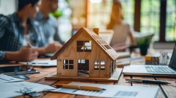 A detailed wooden house model sits on a table as a team discusses real estate and property matters. photo