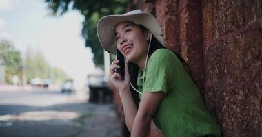 Handheld selective focus shot, Relaxed young woman sits against a brick wall and chatting happily on mobile phone. video