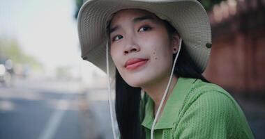 Handheld selective focus shot, Happy young Asian woman sits relaxing on the sidewalk, smiling and enjoying the atmosphere around her. video