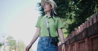 Handheld low angle view shot, Happy woman in a green shirt and blue jeans is walking on the sidewalk next to a brick wall and enjoying her surroundings. video