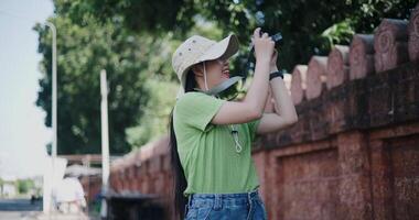 Handheld low angle view shot, Happy young Asian woman standing enjoying the surrounding view while taking photos with her camera. video