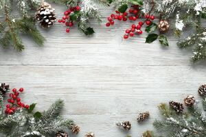 Christmas frame with pine cones, berries and holly branches on a white wooden background photo