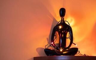 Black figurine of meditating figure adorned with colorful lights against warm wall backdrop photo