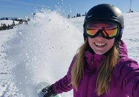 A woman wearing a helmet and goggles on a snowboard photo