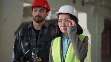 constructores multiétnico negocio trabajadores japonés inspector trastornado malo proyecto fallar trabajo frustrado asiático mujer casco de seguridad tomar apagado lentes ingenieros hablar caucásico hombre discutir edificio problema construcción video