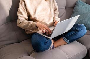 Woman Using Laptop Computer Sitting on Sofa, Relaxing at Home with Electronic Device. Digital Technology and Remote Work Concept. photo