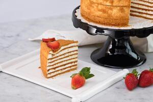 Elegant Medovik Honey Cake decorated with fresh strawberries and blueberries and displayed on a black cake stand closeup side view of classic cafe dessert photo