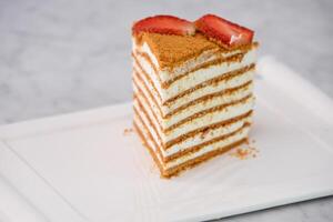 Slice of Classic Medovik Honey Layer Cake layers of honey sponge and creamy filling topped with strawberry slices served in tray isolated on grey background closeup side view of classic dessert photo