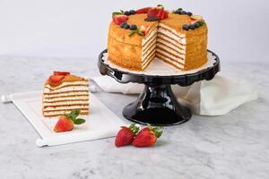 Elegant Medovik Honey Cake decorated with fresh strawberries and blueberries and displayed on a black cake stand closeup side view of classic dessert photo