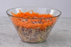 Colorful Carrot and Cabbage Coleslaw Salad in a glass bowl featuring shredded green and red cabbage with a creamy sauce, top with shredded bright orange carrots side view of colorful classic salad photo