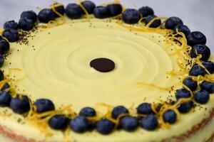 Elegant Lemon Blueberry Layer Cake a vibrant yellow lemon frosting, decorative topping of fresh blueberries, lemon zest, and poppy seeds isolated on grey background closeup top view of baked dessert photo
