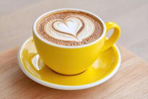 Yellow coffee cup filled with latte art featuring a heart design, placed on a wooden surface, showcasing a warm and inviting beverage experience in a cozy atmosphere photo