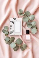 Elegant flat lay composition featuring a perfume bottle, blank card, and eucalyptus leaves arranged on soft pink satin fabric, creating a serene and stylish atmosphere for branding photo