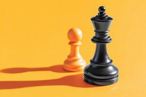 Black king chess piece stands tall beside orange pawn on vibrant yellow background, casting long shadows, symbolizing strategy and competition in the game of chess photo