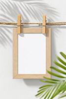 Blank wooden frame hanging on a rope with clothespins, surrounded by green leaves, creating a natural and inviting atmosphere for design and decoration purposes photo