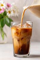 Iced coffee beverage being poured into a clear glass filled with ice, showcasing rich colors and textures, with a soft floral background enhancing the refreshing drink experience photo