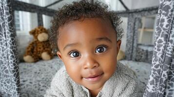 A black baby in a light-colored jumpsuit crawls around his crib with a curious look photo