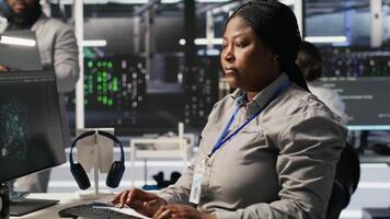 Data center programmer coding on PC, doing software updates for AI visualization systems. African american woman in server room optimizing infrastructure using artificial intelligence, camera A video