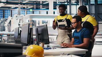 Colleagues troubleshooting solar equipment from computer station in a sustainable industrial factory. Black engineering team handles CAD software adjustments for production line. Camera B. video
