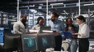 Smiling engineering team in server room reviewing infrastructure diagnostics on devices. IT professionals in data center analyzing performance data to maintain system integrity and uptime, camera A video