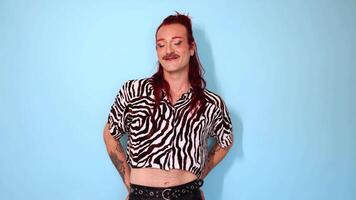 Non-binary person with red hair and mustache smiling on blue background video