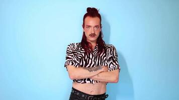 Non-binary person with arms crossed posing on blue background video