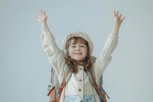 Joyful young girl with arms raised in excitement, wearing a hat and backpack photo