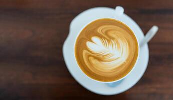 Steaming cup of latte with latte art on a wooden table in a cozy cafe setting. photo