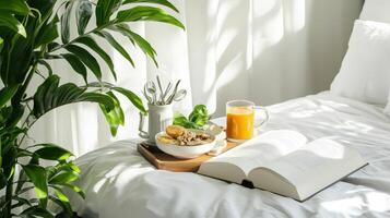 A book, bowl of cereal and orange juice are on a bed photo