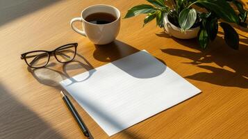 A blank paper, pen, glasses and a plant on a wooden table photo