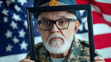 An old man in glasses holding a picture frame with an american flag in the background photo