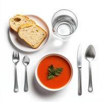 A bowl of tomato soup, bread and silverware on a white table photo