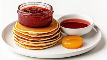 A stack of pancakes with jam and a bowl of fruit photo