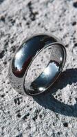Beautiful silver wedding band on textured stone surface reflecting light in natural outdoor setting photo