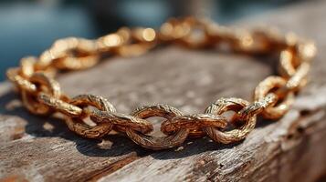 Shiny gold chain bracelet resting on a rustic wooden surface near water during daylight photo