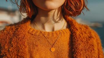 Woman with short red hair wearing an orange sweater and necklace during a sunny day by the water photo