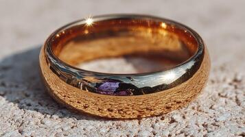 Golden wedding band resting on a textured surface reflecting sunlight in an outdoor setting during the daytime photo