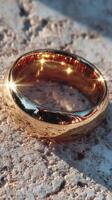 Elegant gold wedding ring resting on textured stone surface in natural light, capturing reflections and brilliance photo