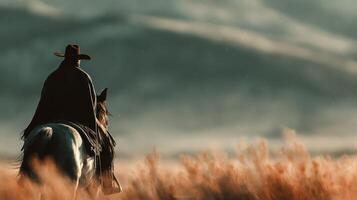Cowboy riding horse through tall grass at sunset, surrounded by mountains in the background photo