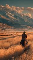 Horseback rider traverses golden grasslands against snow-capped mountains during sunset in a breathtaking landscape photo