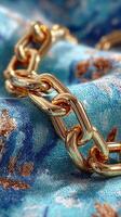 Close-up of a shiny gold chain resting on a blue floral fabric with intricate patterns in soft daylight photo