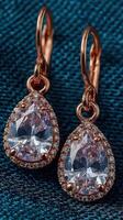 Elegant droplet earrings showcasing sparkling crystals set in rose gold, placed on a textured teal fabric background photo