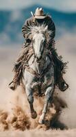 Cowboy riding a spirited gray horse across a dusty field under a vast blue sky photo