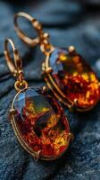 Elegant amber earrings with intricate gold settings displayed on a textured stone background photo