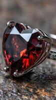 Heart-shaped red gemstone ring with intricate design displayed on a textured surface photo
