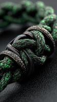 Intricate green and black braided cord tied with metallic rings laid on a leather surface photo