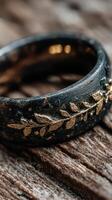 Intricate black and gold ring adorned with detailed leaf patterns resting on rustic wooden surface photo