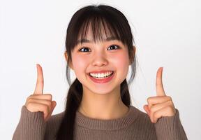 A joyful young girl in a cozy sweater pointing upward with a beaming smile against a bright, neutral background photo