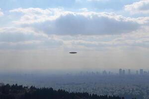 A large object flying over a city with trees in the background photo